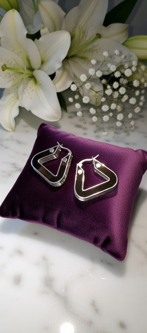 Silver hoop earrings on a purple cushion with white flowers in the background
