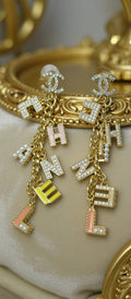 Chanel earrings with letter charms on a gold background