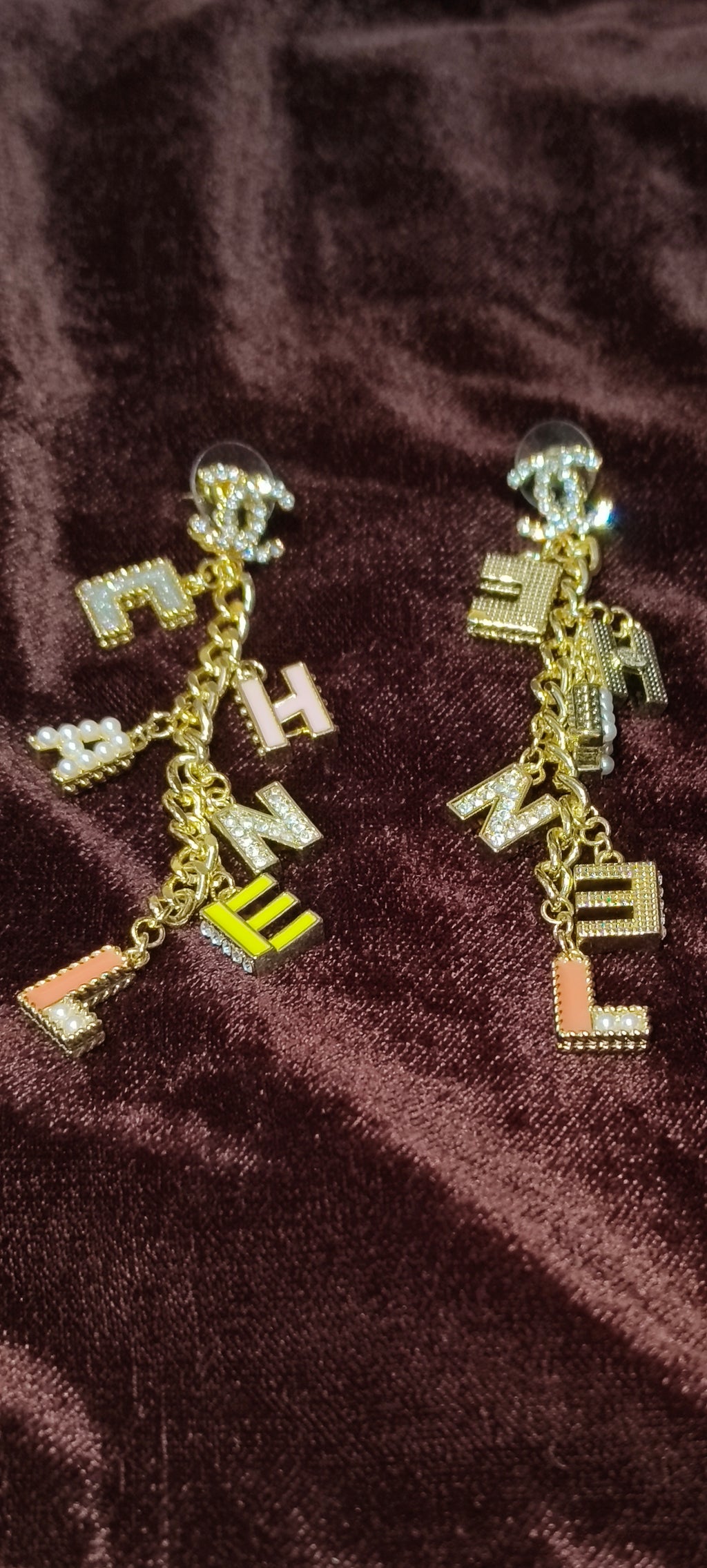 Gold earrings with letter charms on a brown fabric background