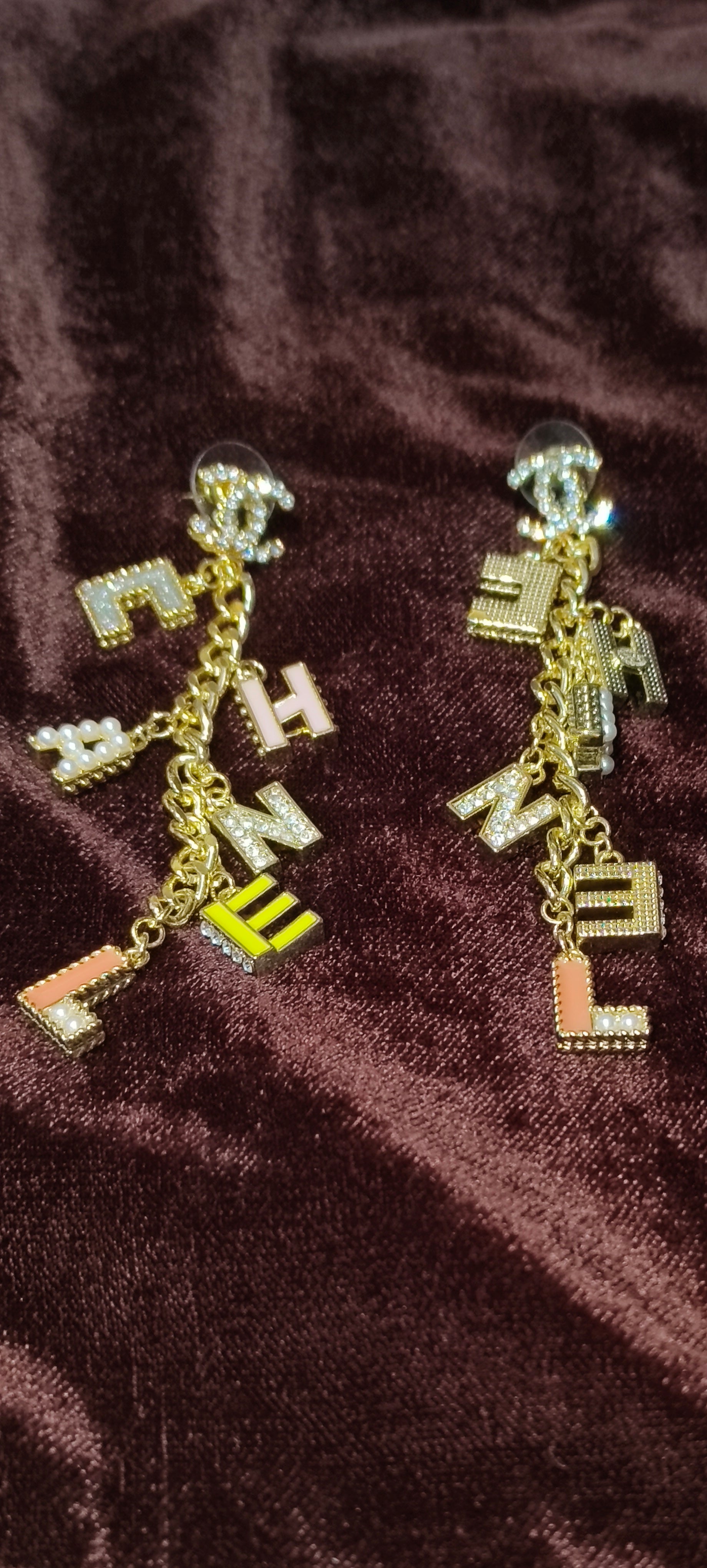 Gold earrings with letter charms on a brown fabric background